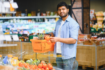 Young indian man choosing tomatoes in grocery store