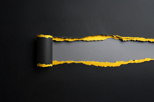 A creative and conceptual abstract background featuring a horizontal tear in a black paper surface, revealing vibrant yellow and textured gray layers underneath. The peeling paper adds a dynamic effec - Powered by Adobe