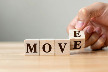 Hand turning wooden block to reveal letter e completing the word move
