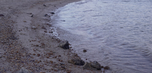 Close up view of rocky sandy shoreline with small waves gently washing ashore creating a peaceful nature background

