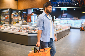 Young indian man walking through supermarket holding shopping basket