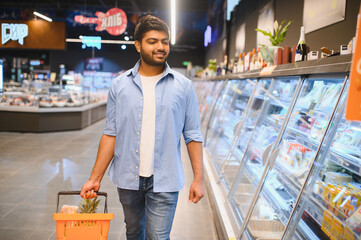 Young indian man choosing frozen food in supermarket