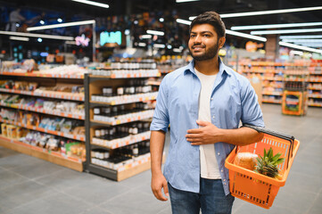 Young indian man holding shopping basket in supermarket