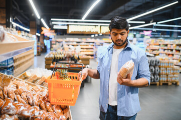 Young indian man choosing bread in supermarket bakery section