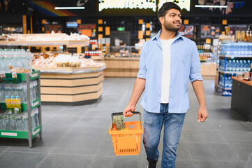 Indian man holding shopping basket walking in supermarket
