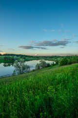 A tranquil evening view of a calm lake, with a bright sunburst and lens flares over the water, and a green shoreline with a distant treeline