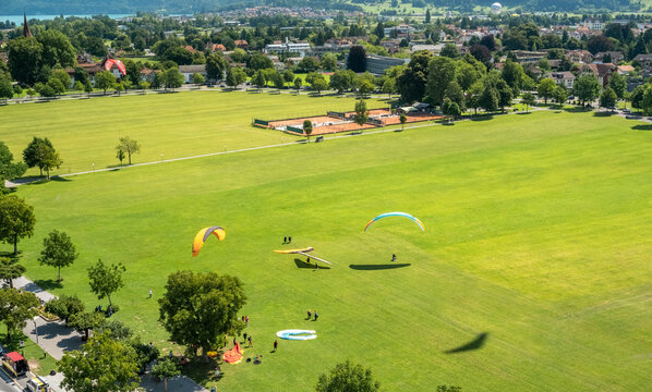 Paragliders Landing on a Large Green Field in Scenic Town of Interlaken, Switzerland - Powered by Adobe