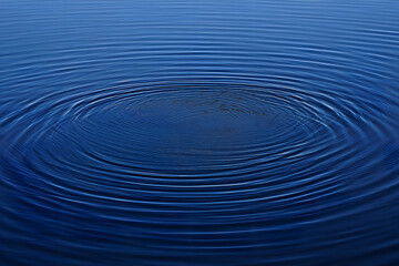 Abstract background of deep blue water with concentric circles and ripples from a central impact. Serene and tranquil liquid surface.