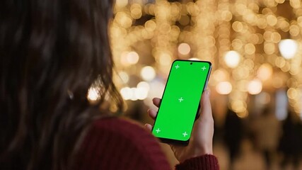A woman holds a greenscreen phone against blurred lights - Powered by Adobe