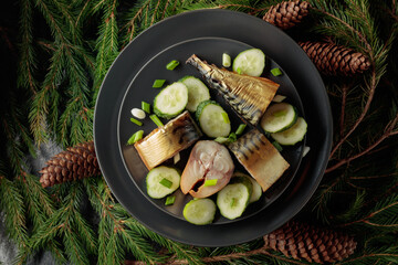 Smoked mackerel with fresh cucumber and green onions on a black plate.