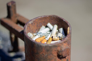 Cigarette Butts Collected in Rusty Metal Container at Outdoor Location During Daytime