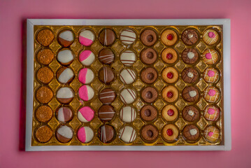 Assorted colorful cookies in golden tray box on pink background, top view