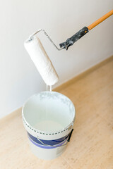Paint roller dripping white paint into bucket during home renovation