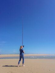 Barefoot woman on the seashore, holding a fishing rod, under a cloudless blue sky