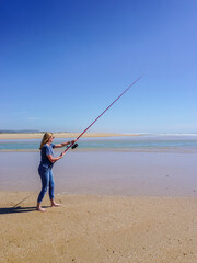 Barefoot woman on the seashore, holding a fishing rod, under a cloudless blue sky