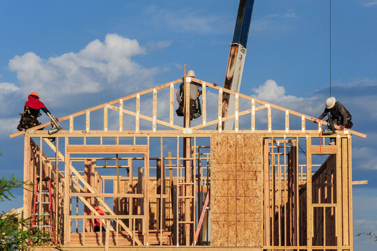 Construction crew works on wooden framing of a residential house, using crane support for roof trusses, representing home building and structural carpentry operations