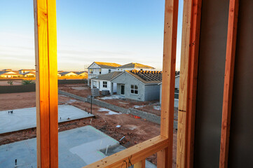 View from framed window of a house under construction overlooking single-family homes in a new subdivision, representing residential building and housing development