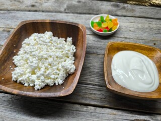 Homemade traditional cottage cheese organic dairy product in wooden bowl, next to it is a cup of sour cream