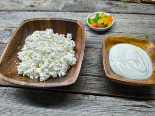 Homemade traditional cottage cheese organic dairy product in wooden bowl, next to it is a cup of sour cream