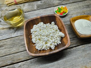Homemade traditional cottage cheese organic dairy product in wooden bowl, next to it is a cup of sour cream