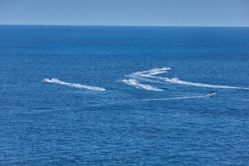 Naklejka premium Several jet skis and a motorboat carve dynamic trails across a calm, open sea under a clear blue sky. movement, recreation