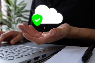 Businesswoman working at desk with computer while holding a cloud icon with a shield. Cloud file security concept.