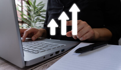 Woman in front of her laptop pointing at an ascending graph icon made of arrows