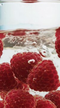extreme close-up macro video of plump, glistening, ruby-red raspberries gently dropping into crystal-clear water in a glass bowl, creating elegant ripples. ultra-shallow depth of field. soft natural
