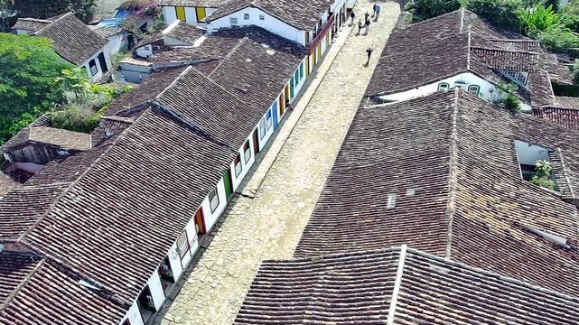 Aerial view of the historic town of Paraty, Rio de Janeiro, Brazil. Featuring colonial architecture, traditional tiled roofs, and a classic cobblestone street with people walking.