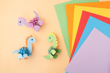 Colorful dinosaur crafts from painted pinecones and cardboard on orange background with stack of paper. Great for kids workshops, craft supply stores, creative learning and DIY kit promotion,