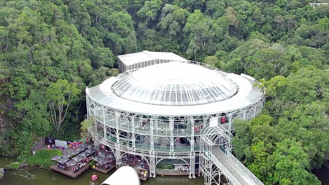 Aerial view of the &Oacute;pera de Arame (Wire Opera House), a famous tourist landmark in Curitiba, Brazil. The structure is set in the Quarrying Park, surrounded by a lake and lush green forest.