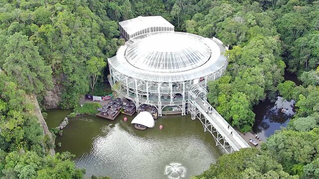 Aerial view of the &Oacute;pera de Arame (Wire Opera House), a famous theater and tourist landmark in Curitiba, Brazil, nestled amidst a lush green forest and a lake in Quarrying Park.