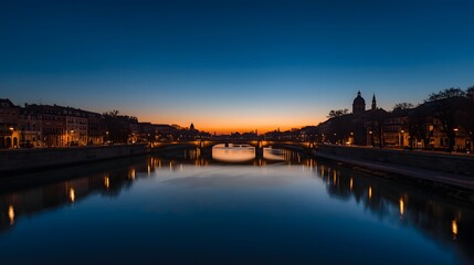 Fototapeta premium Scenic evening view of illuminated city riverfront with calm water reflections, glowing street lights, and beautiful twilight sky creating romantic and tranquil urban atmosphere