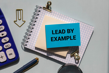 Lead by example message written on ripped torn purple paper on blue background.