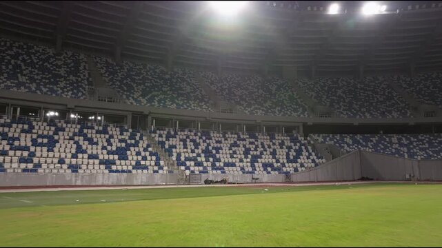 empty stadium or race track seats. Rows and blue and white seats without viewers and spectators. Evening shot of empty football stadium. Soccer Arena drone aerial view. Football Stadium moving view. 