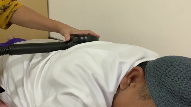 An elderly man undergoes Therapeutic Magnetic Stimulation (TMS) therapy at a hospital, assisted by a professional nurse.