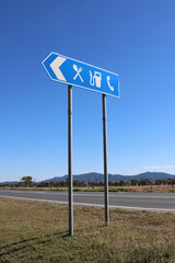 Blue road sign for a rest area with food and petrol gas fuel facilities against a blue sky background