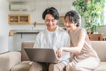 マイホームでパソコンを使う若いアジア人夫婦（資産運用・ネットショッピング）
