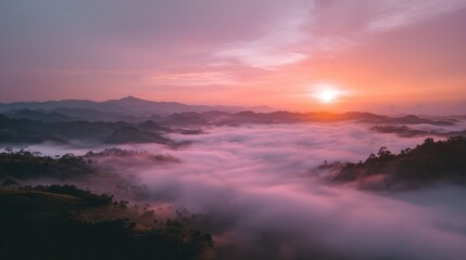 Sunrise over a valley shrouded in mist.  A vast landscape of rolling hills and mountains is bathed in the warm hues of a sunrise.  