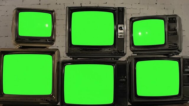 Six old televisions with green screens are stacked in front of a white brick wall