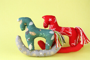 Two Tilda-style horses sewn from fabric. Concept - Christmas toy, Christmas tree decoration, New Year theme. Yellow background, horizontal photo. There is space for text.