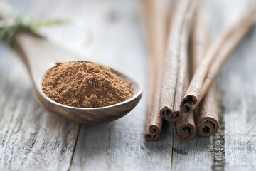Ground cinnamon on a wooden spoon with cinnamon sticks on a rustic table. Ideal for healthy diets, organic food, and real food concepts