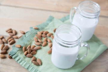 Two glasses of creamy almond milk with scattered almonds on a green cloth. Perfect for a healthy diet, organic food, and a real, plant-based lifestyle