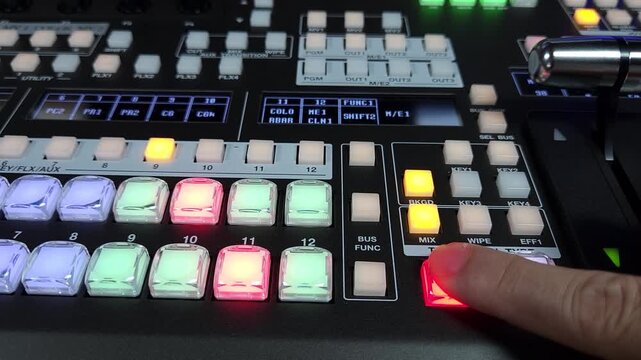 Close up of a video switcher control panel showing a hand pressing a red-lit button during live production operation.