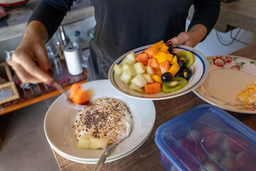 woman preparing a bowl with yogurt mango in a healthy breakfast with cereal and honey, grapes, kiwi, banana, mango and papaya