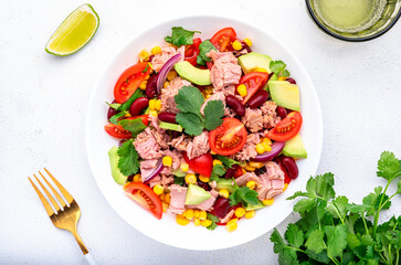Mexican style salad with canned tuna, avocado, corn, red beans, cherry tomatoes and cilantro, white table background, top view