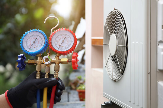 Air conditioning electrical technician using manifold gauge measuring tool checking refrigerant pump filling home air conditioner and maintenance heat fix repair and clean outdoor compressor unit.