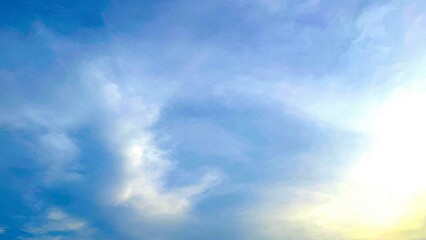 Sunshine breaks through soft white clouds in a beautiful light blue sky background