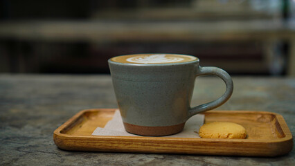 Cup of hot latte coffee with beautiful latte art topped with a butter cookie