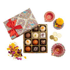 A vibrant collection of traditional indian sweets and chocolates in a decorative gift box, accompanied by festive diyas, flowers, and gold coins, perfect for celebrations like diwali.